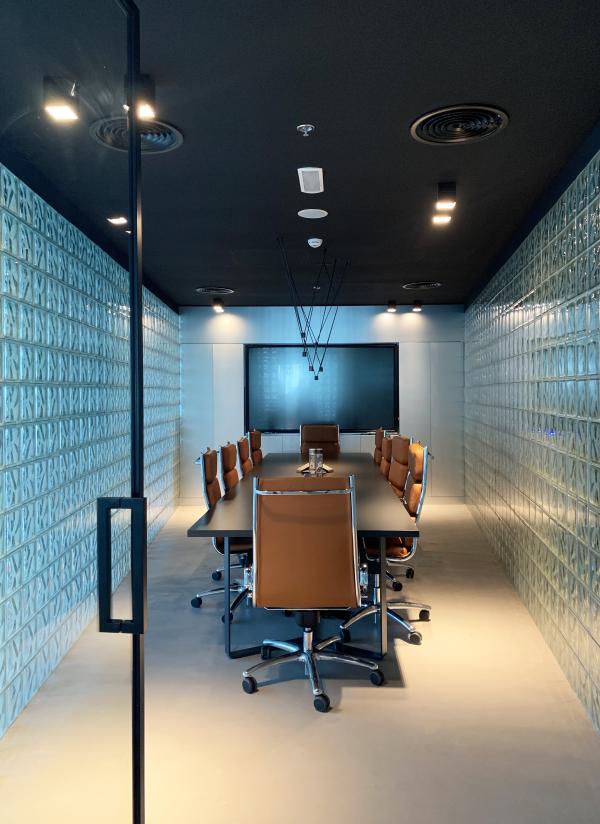Glazed meeting room with a glass-block wall, a monitor, and orange task chairs, Man Corporate Office, Binary Tower by Omniyat, Business Bay, Dubai