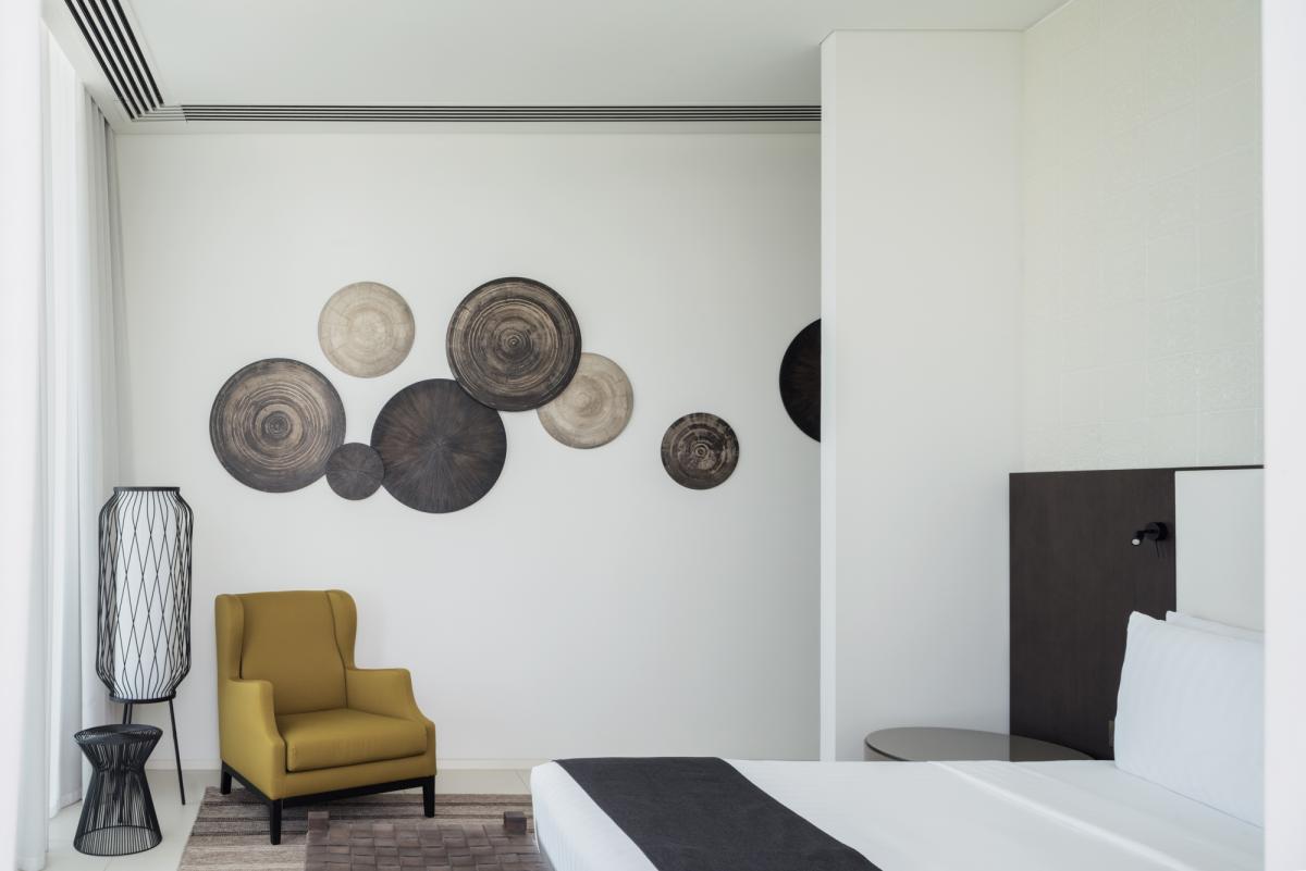 Bedroom corner with wall-mounted disc decor and a mustard armchair, Oberoi Resort, Ajman